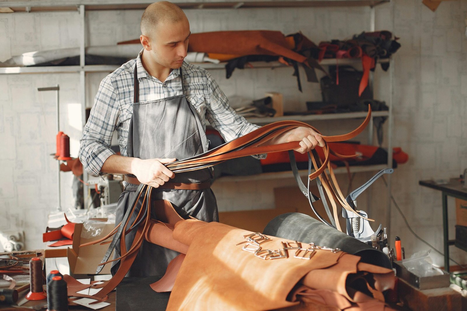 A focused leather craftsman inspects materials in a well-lit workshop.