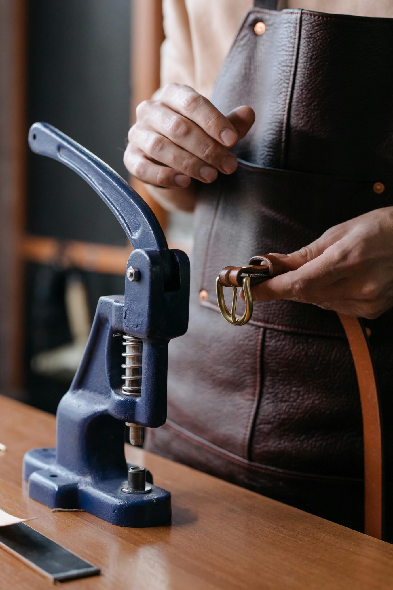 Close-up of a craftsman using a hand press puncher on a leather belt with metal buckle.